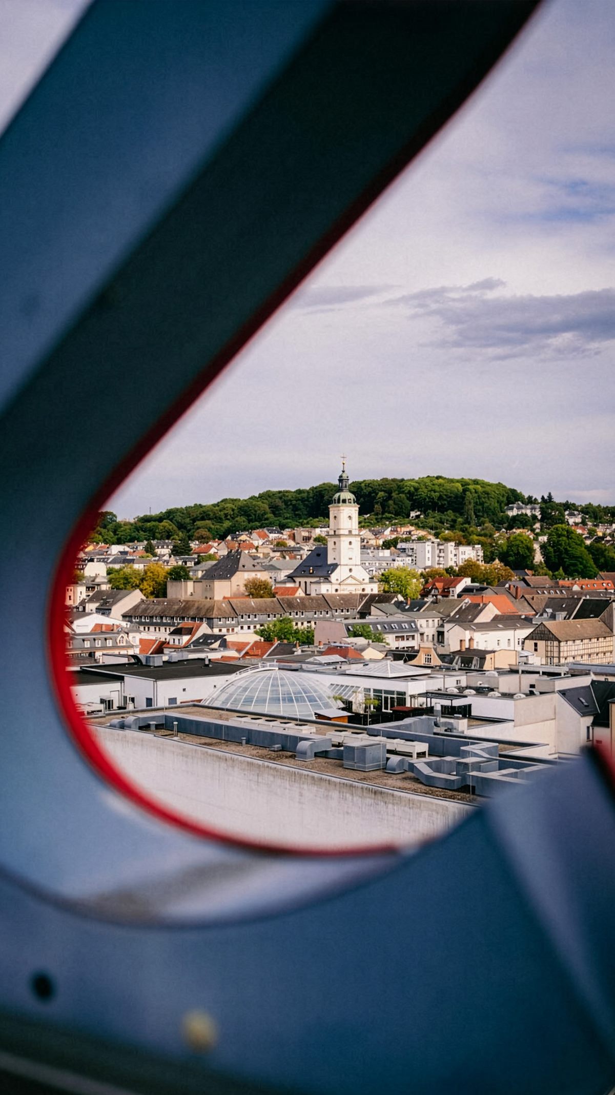 Blick durch die Dachkonstruktion des Handelshofs über die Dächer von Gera bis zum bewaldeten Hügel mit Kirchturm