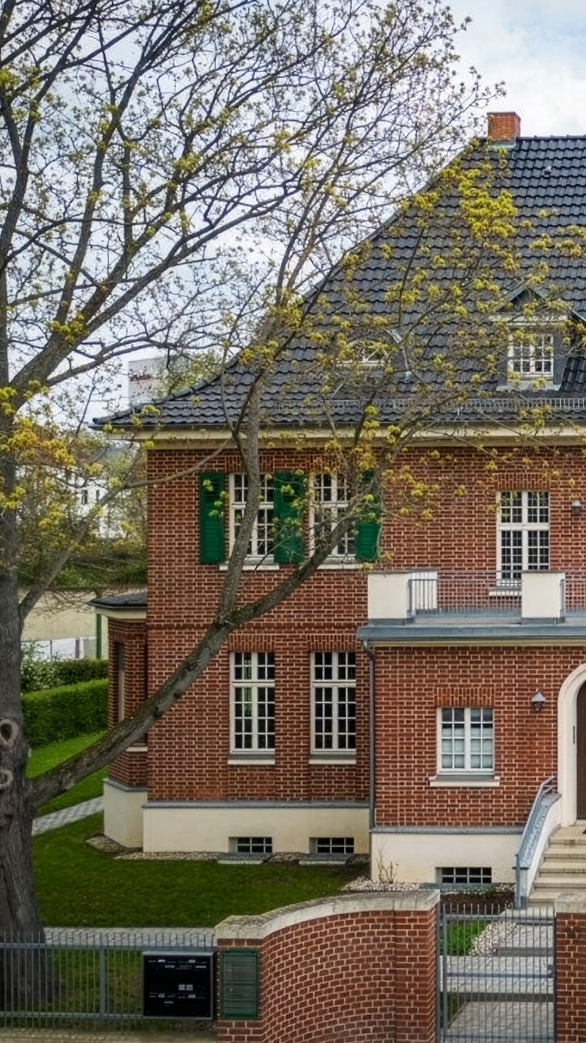 Backsteinvilla Mazur mit grünen Fensterläden hinter kahlen Bäumen