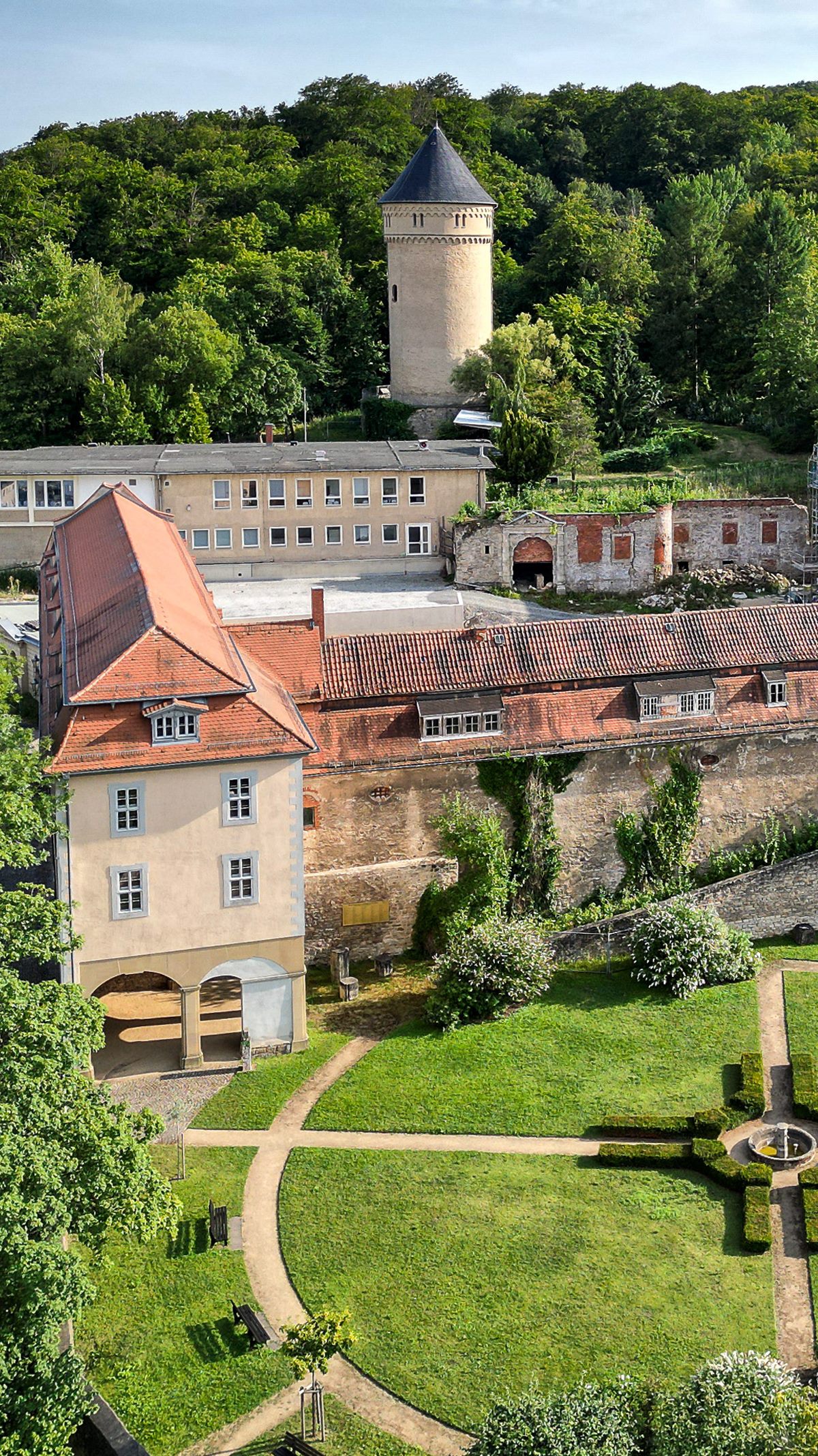 Schloss Osterstein mit rundem Turm über dem bewaldeten Hang, davor der Barockgarten