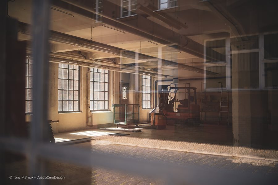 Sonnendurchflutete Fabrikhalle mit historischen Maschinen, durch eine Fensterscheibe fotografiert