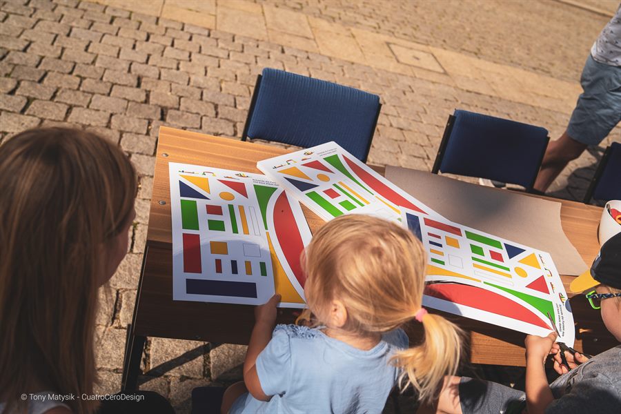 Mutter und Kind betrachten eine bunte geometrische Bauhaus-Bastelvorlage auf dem Marktplatz